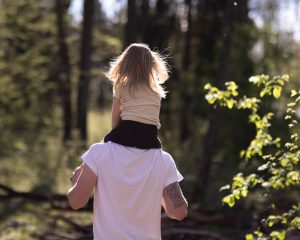 Ein Bild eines Vaters mit seiner Tochter auf der Schulter im Wald bei Gegenlicht.