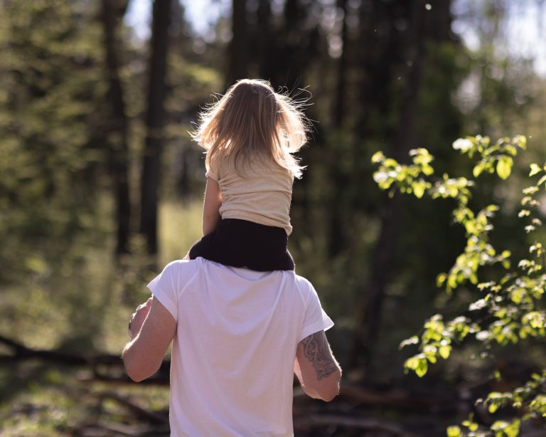 Ein Bild eines Vaters mit seiner Tochter auf der Schulter im Wald bei Gegenlicht.