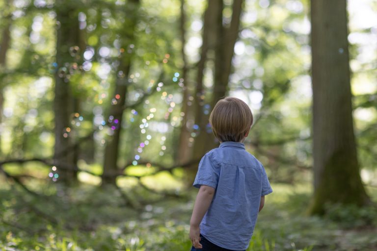 Ein Kind steht im Wald und spielt mit Seifenblasen.
