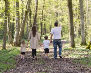 Eine vierköpfige Familie geht Hand in Hand im Wald spazieren.